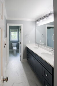 Small bathroom remodel with dark double-sink vanity, large wall mirror, white hexagonal tile flooring, and light gray walls.